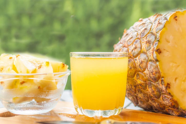 Glass of pineapple juice next to fresh pineapple